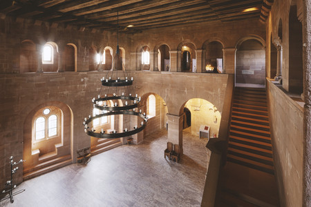 Großer, zweistöckiger Stein-Saal mit Kronleuchter, Fenstern und einer Treppe